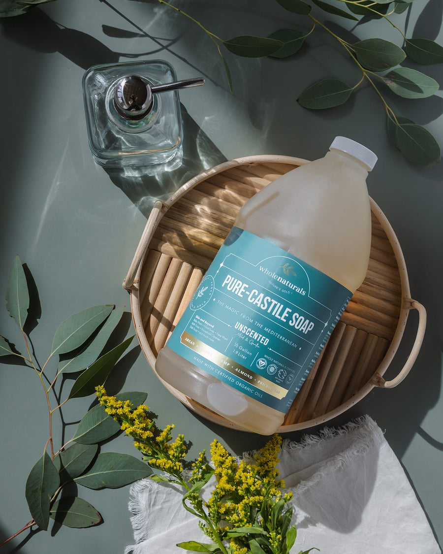 Bottle of Pure-Castile Soap in a woven basket with eucalyptus and a glass soap dispenser